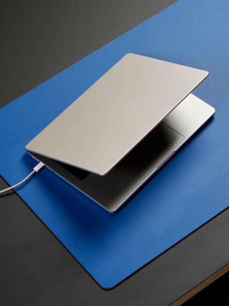 Aerial view of a linoleum table with a Faust large-format PAD Mat in 4181 Midnight Blue serving as a working surface for a laptop