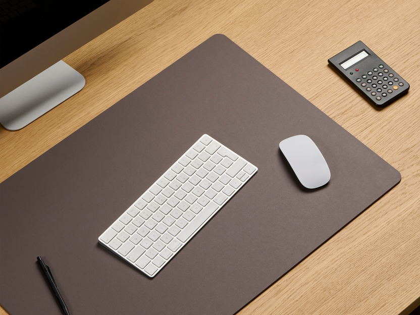 Areal view of an oak veneer office table with a Faust large-format PAD Mat in 4172 Mauve linoleum, along with a keyboard, mouse, computer desktop, and calculator for a practical workspace arrangement